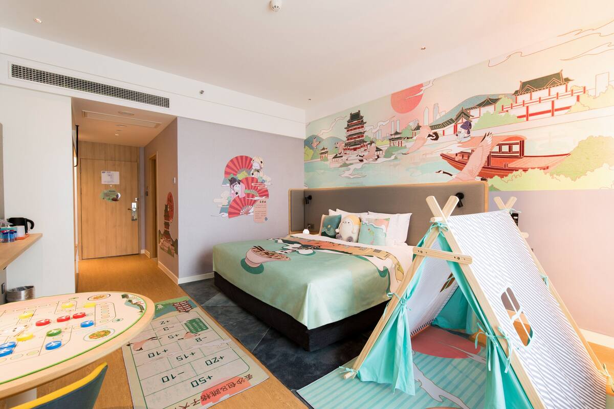 A child-friendly room with a bed, a play area, and a wall mural.