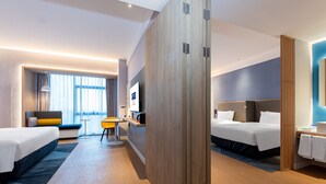 A modern hotel room with two beds, a desk, a chair, and a large window with curtains.