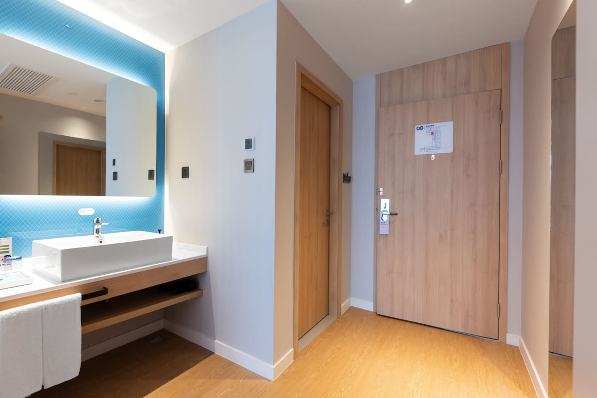 A modern bathroom with a white sink, mirror, and wooden floor.