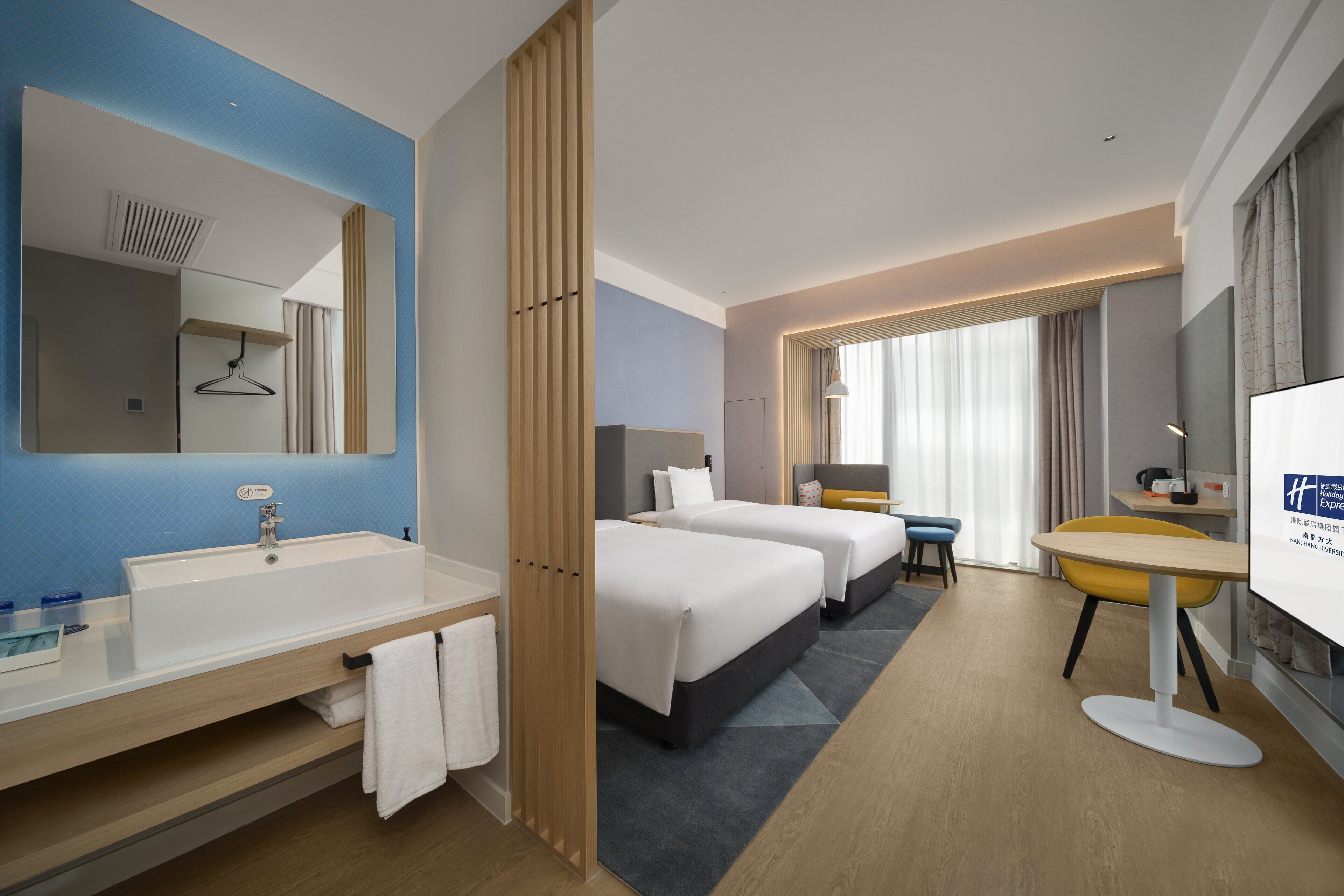 Habitación de hotel con un espejo grande, un lavamanos, dos camas, un escritorio y una silla.