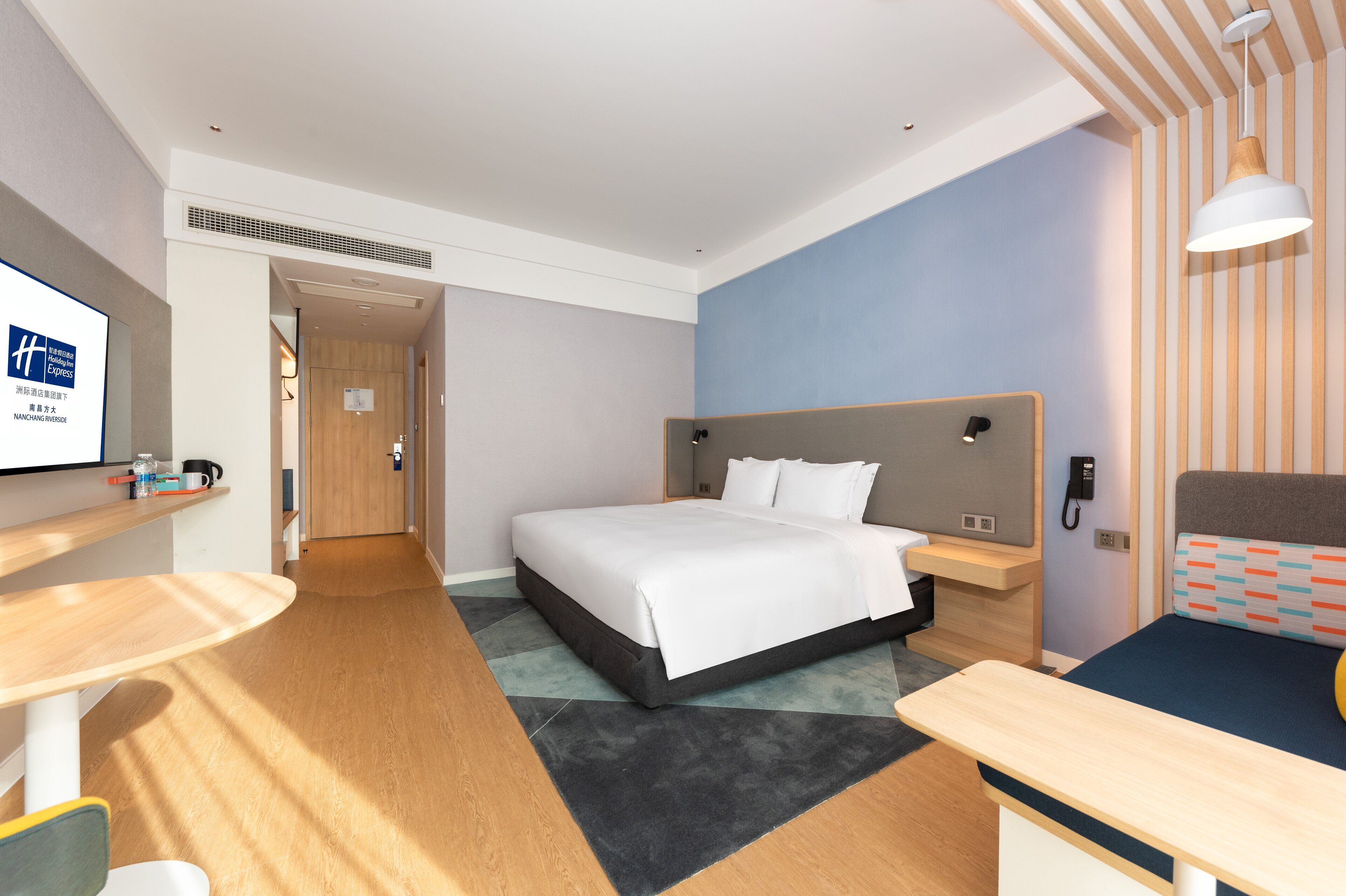 A hotel room with a bed, bedside table, desk, and a TV on a stand.