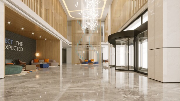 A spacious lobby with a modern design, featuring a high ceiling, a central light installation, and a seating area with sofas and chairs.