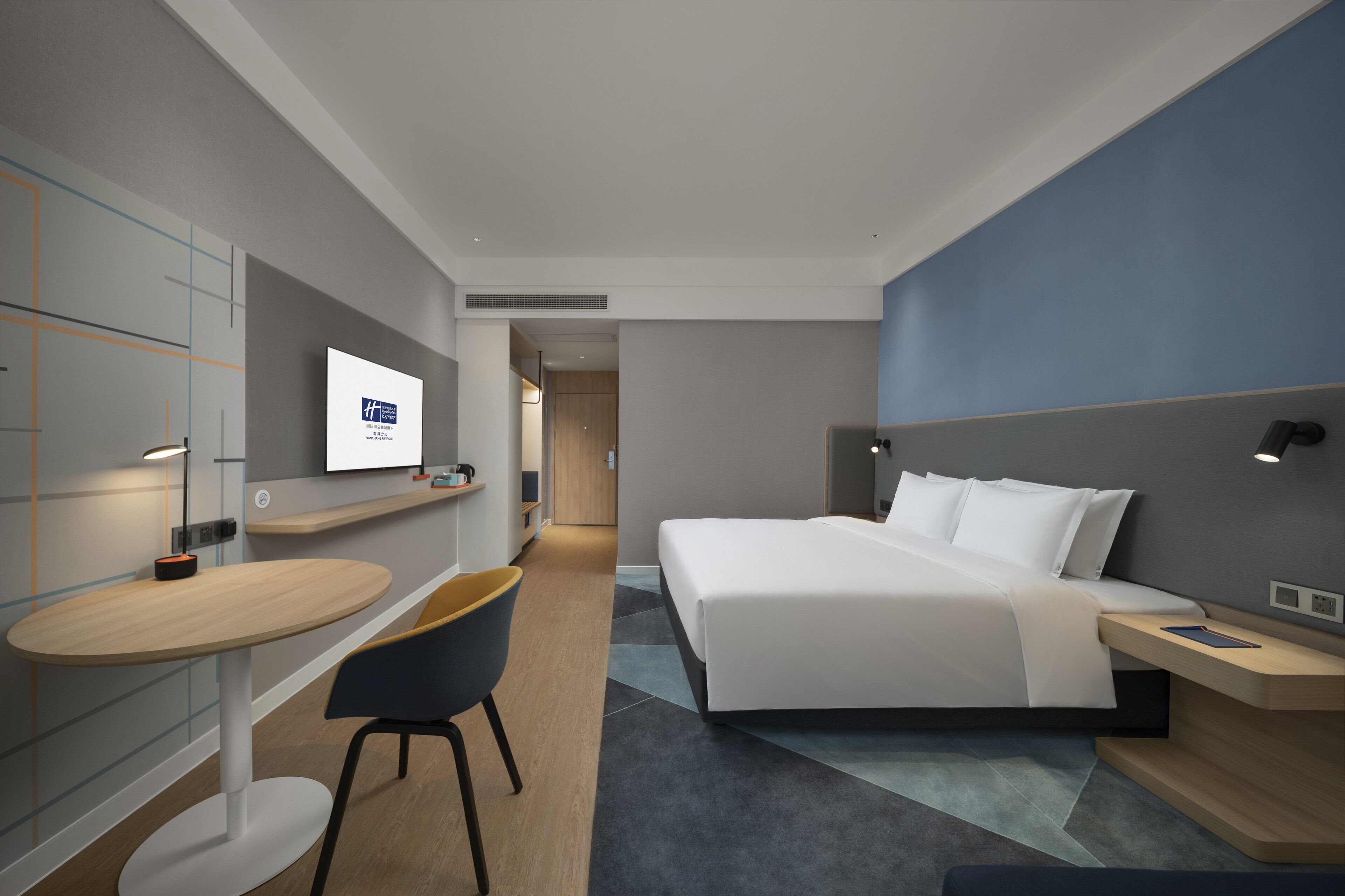 Una habitación de hotel moderna con una cama grande, un escritorio, una silla y un televisor en la pared.