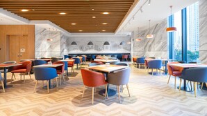 A modern restaurant with wooden ceiling panels, marble walls, and a herringbone floor pattern. Tables and chairs are arranged in a spacious layout.