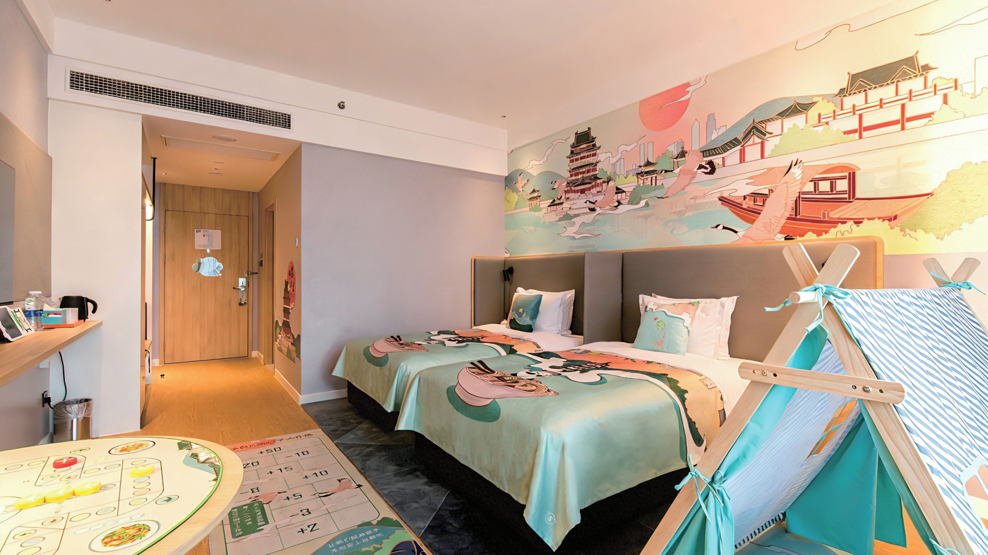 A hotel room with two beds, a wall mural, a small table with a board game, and a teepee-like structure.