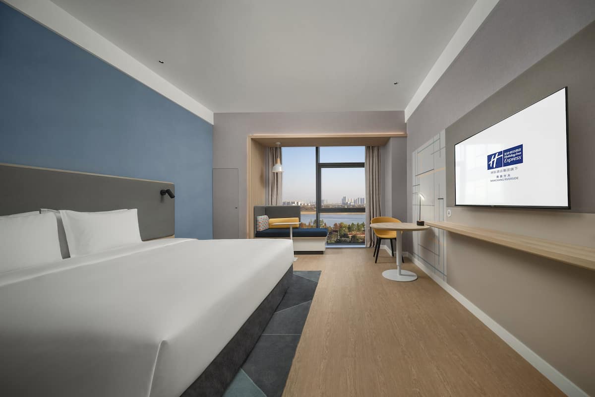 A modern hotel room with a large bed, a desk, and a view of the city.