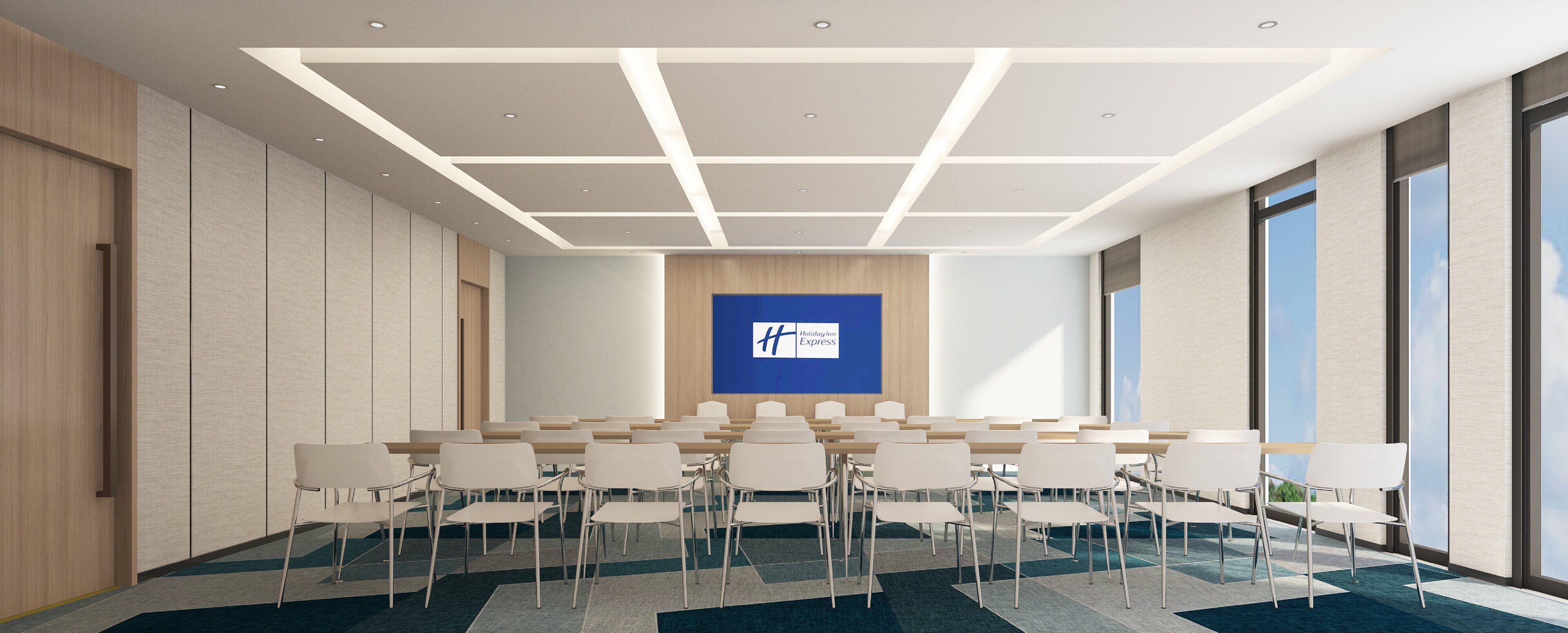 Un salón de conferencias con una gran pantalla que muestra el logotipo de Holiday Inn Express, sillas blancas dispuestas en filas y un diseño moderno de techo.