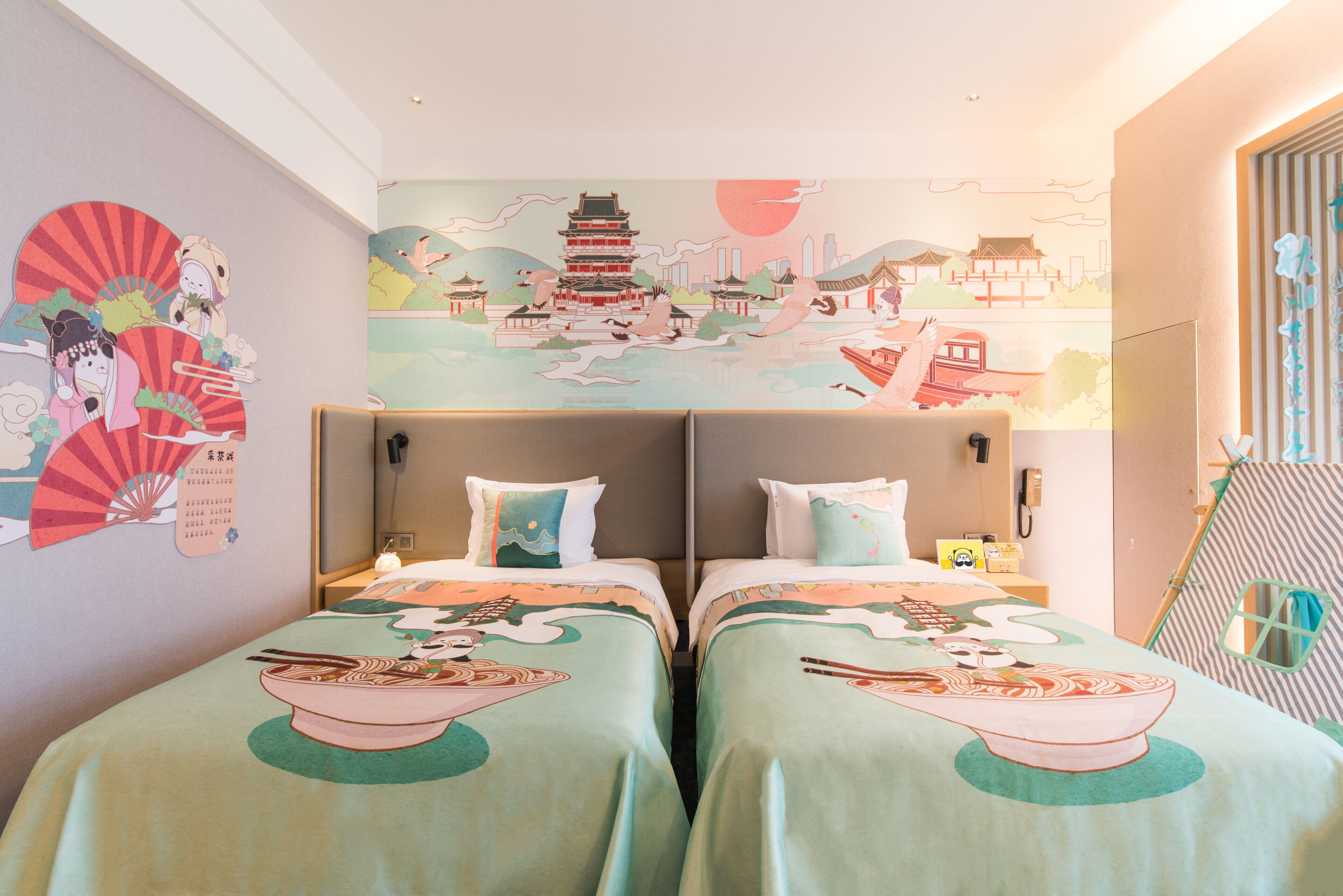 A hotel room with two beds, each with a green bedspread featuring Asian-inspired artwork. There is a mural on the wall depicting a traditional Asian scene.