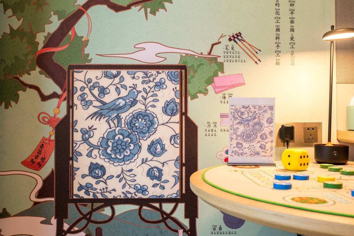 A room with a traditional Chinese-style wall mural, a small easel with a blue and white floral painting, and a table with a game and dice.