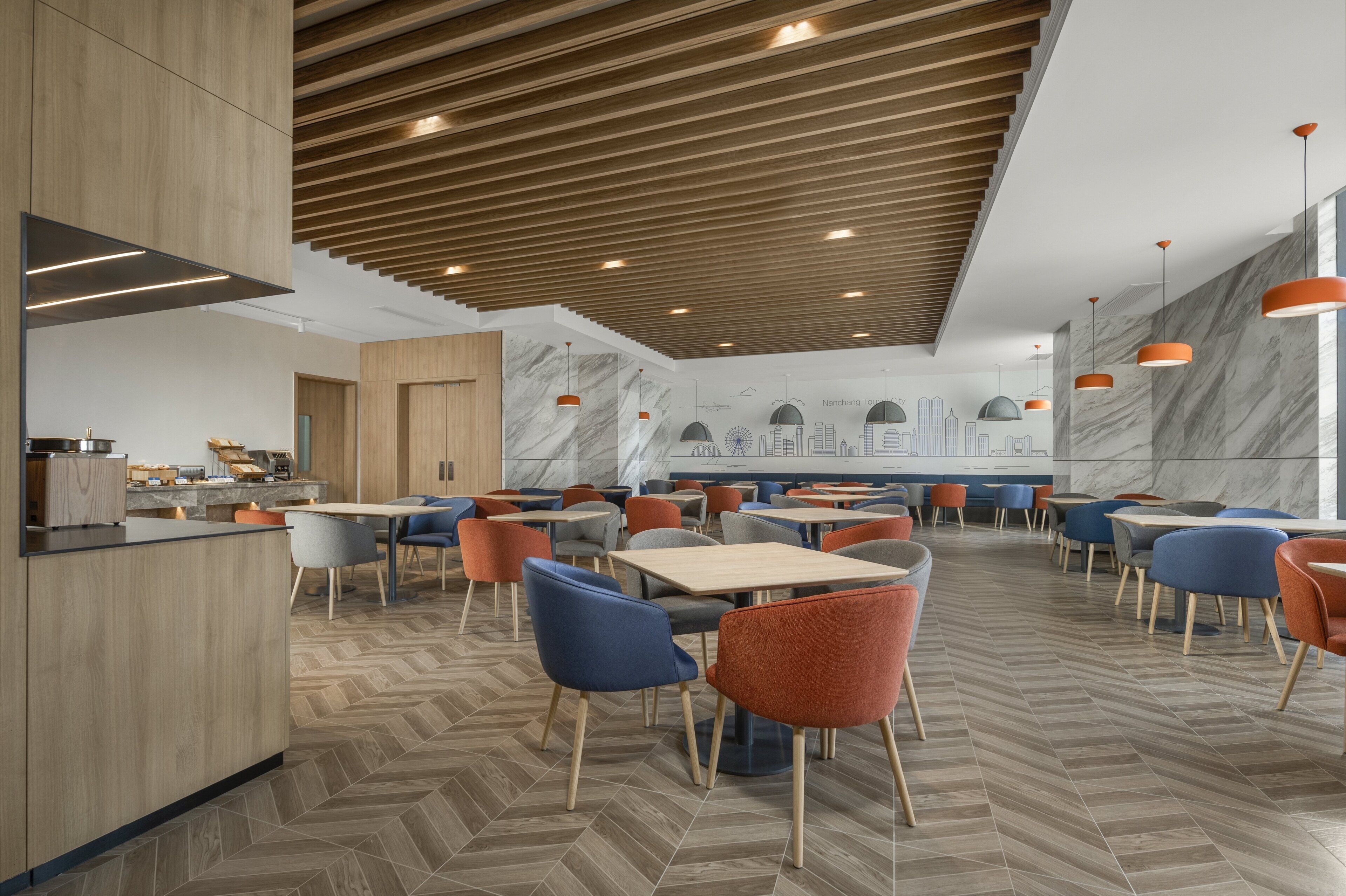 Un restaurant moderne avec des panneaux de bois au plafond, des murs en marbre et un motif de parquet en chevrons. Les tables et les chaises sont disposées pour accueillir les clients.