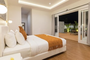 A modern bedroom with a large bed, white bedding, and a view of the outdoor patio area. - Villa Haka Jimbaran by Nagisa Bali (Ungasan)