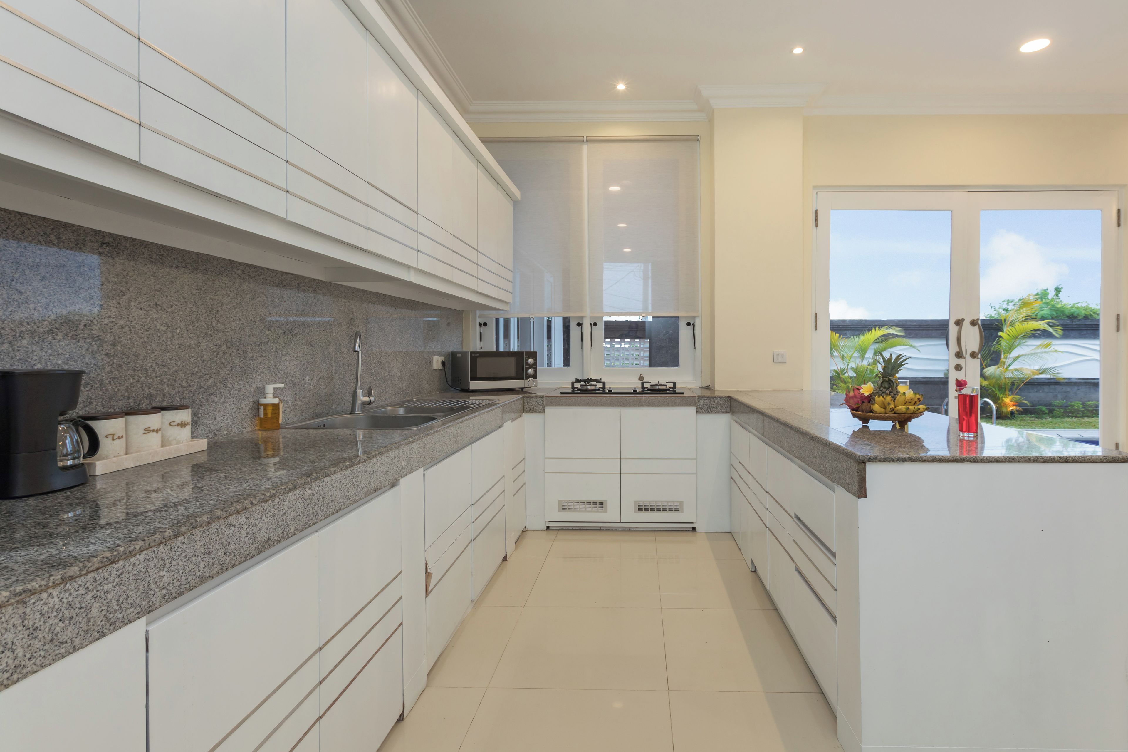 A modern kitchen with white cabinets, granite countertops, a built-in microwave, and a view of the ocean through a sliding glass door.