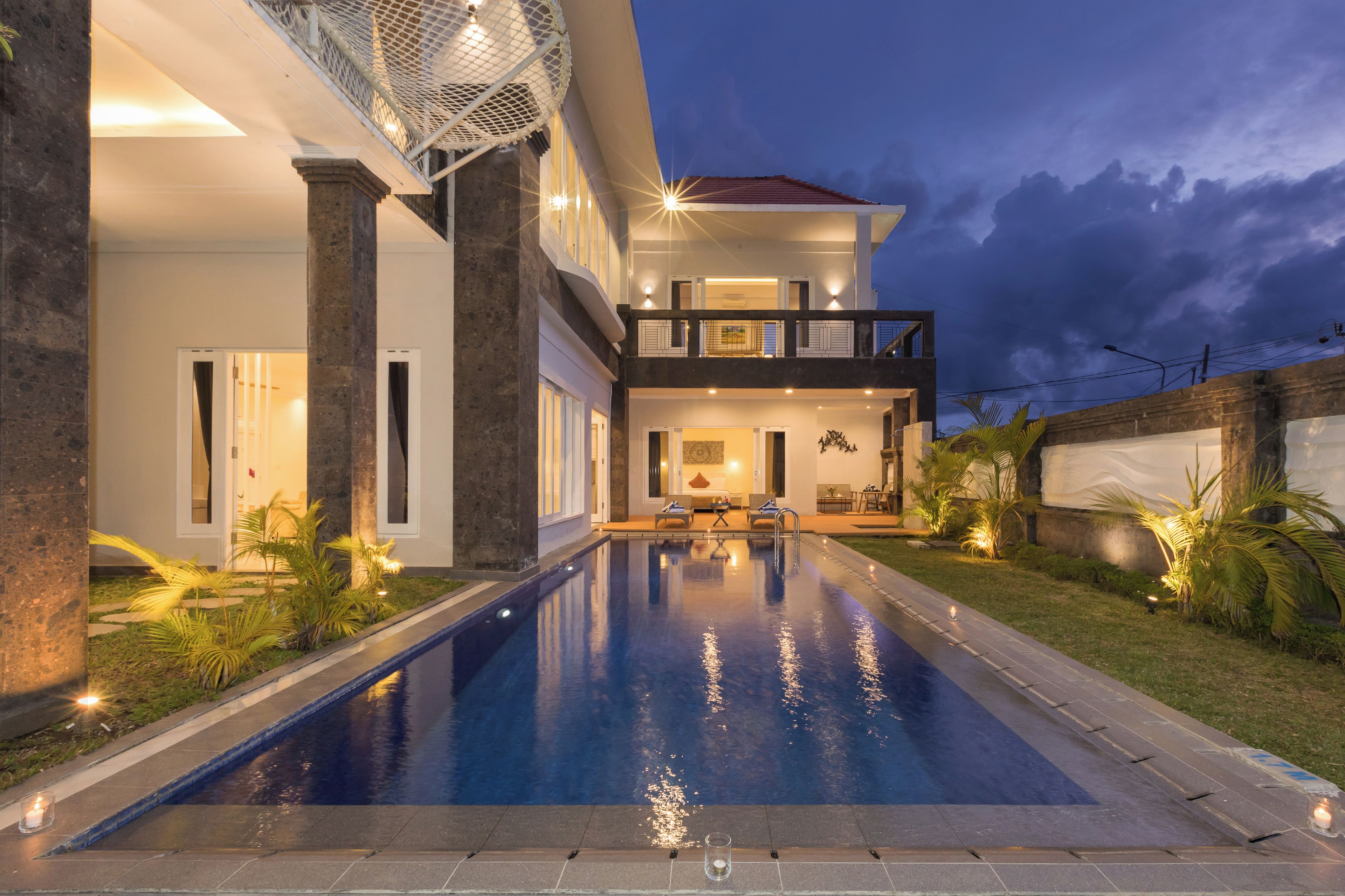 A modern house with a swimming pool, a balcony, and a well-lit interior.