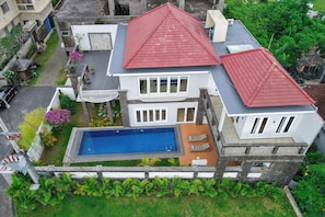 A two-story house with a red roof, a swimming pool, and a garden.