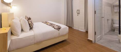 A modern bedroom with a bed, bedside table, and a nightstand. There is a door leading to a bathroom with a toilet and a shower.