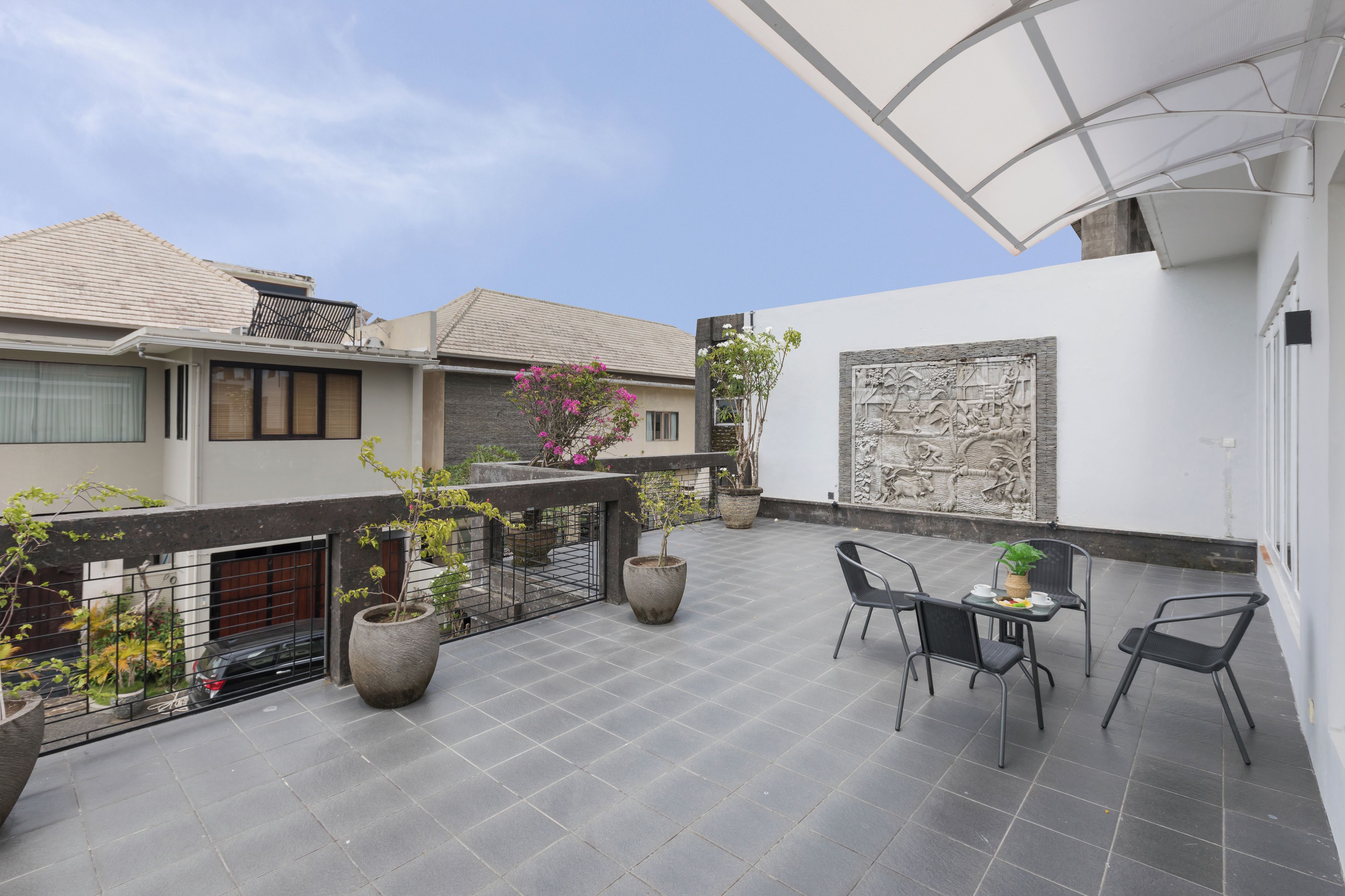 A modern outdoor patio with a dining area, large potted plants, and a decorative wall.