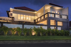 A modern two-story house with a balcony, large windows, and a well-lit facade.