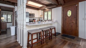 A rustic kitchen with wooden beams, white cabinetry, and a bar area with stools.
