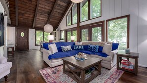 A spacious living room with a high ceiling, large windows, and a cozy blue and white sectional sofa.