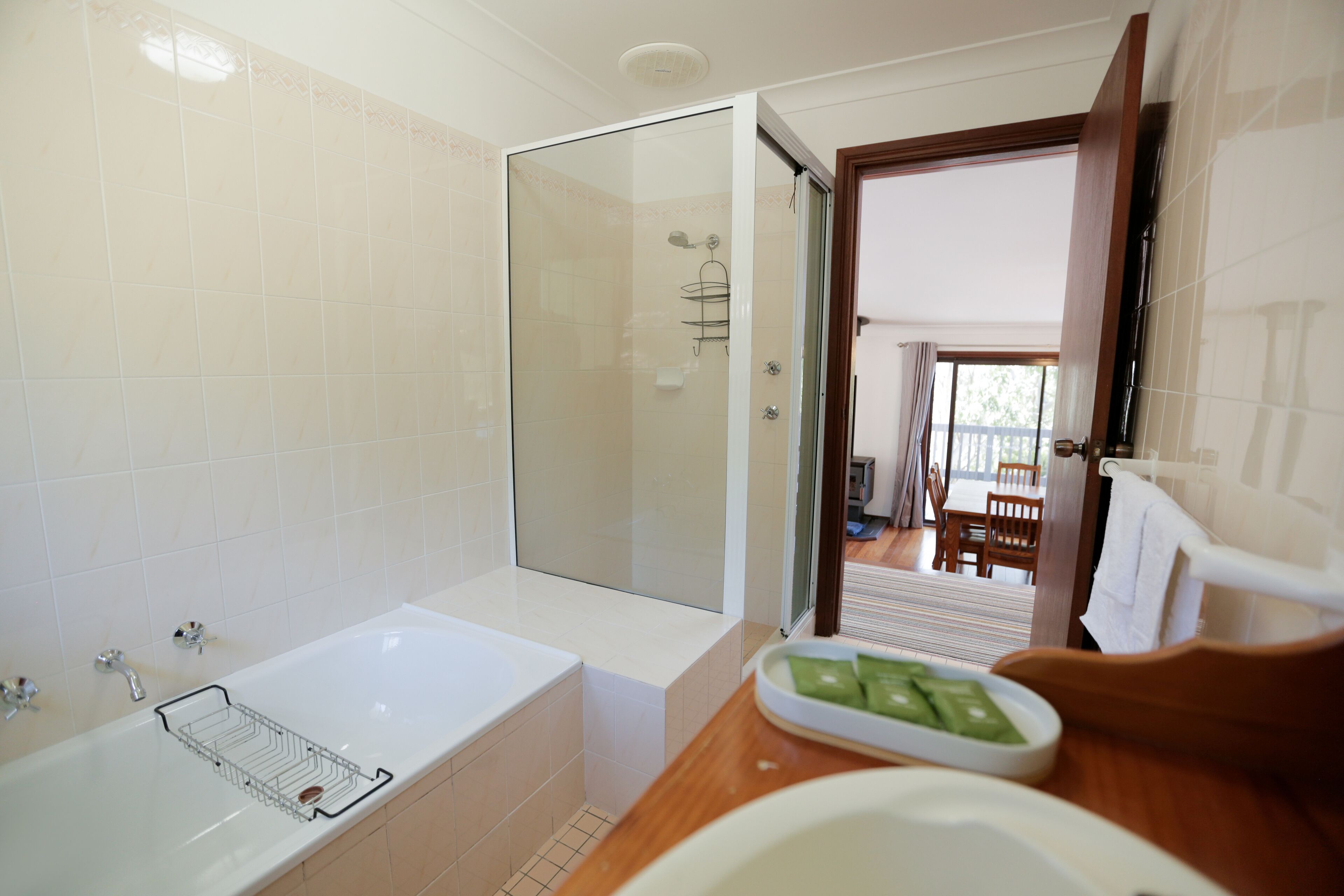 Un baño con bañera, ducha y tocador de madera con lavamanos y jabonera.