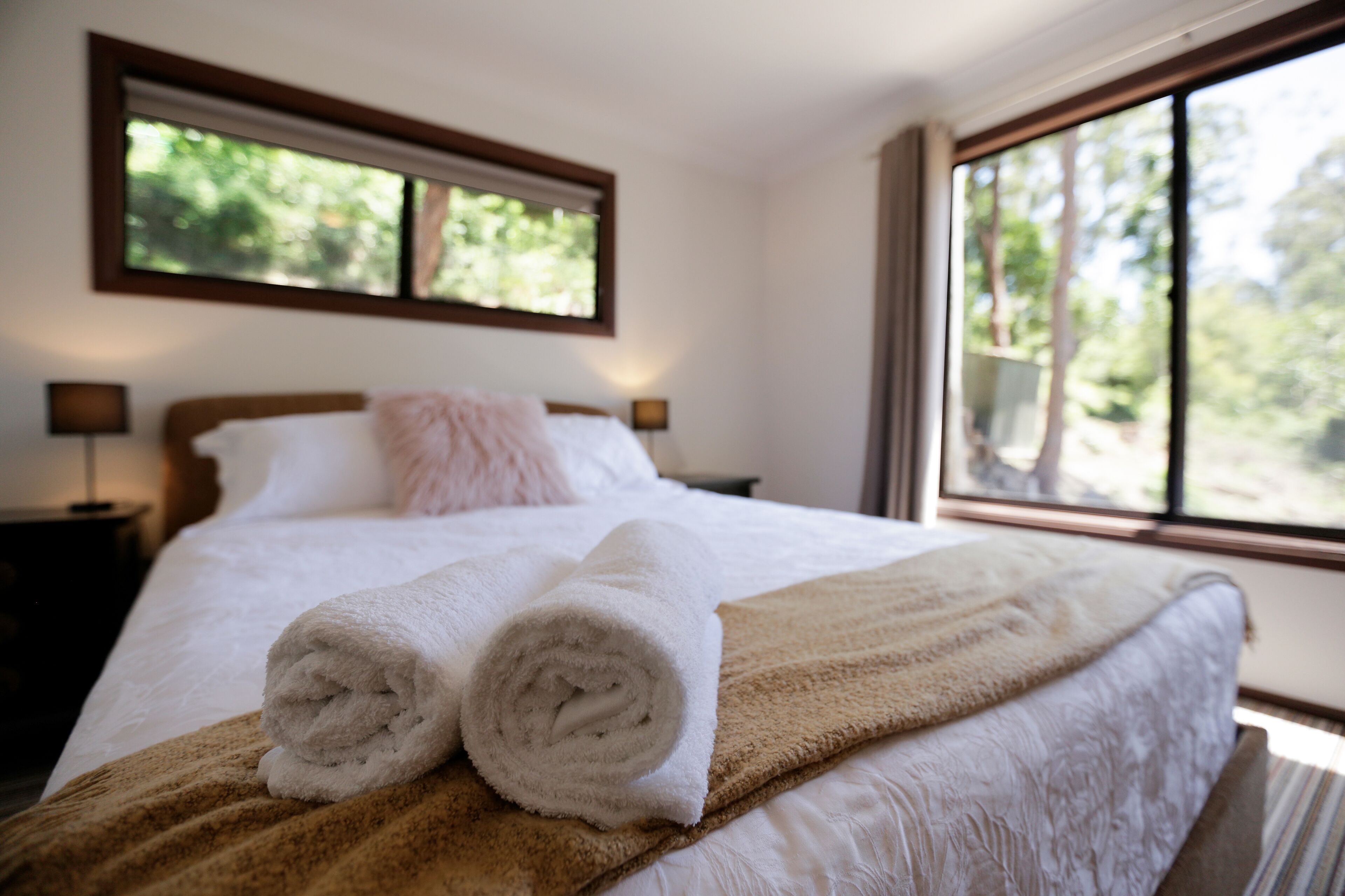 A neatly made bed with rolled white towels, a brown blanket, and a wooden headboard.