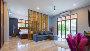 A modern hotel room with a large bed, a sofa, a decorative bamboo wall, and a large window offering a view of the outdoors. - Pool villa  4 BR walking to Beach HV (Hua Hin)