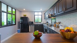 A modern kitchen with dark cabinets, a white brick backsplash, and a wooden countertop. There are two bowls of fruit on the counter. - Pool villa  4 BR walking to Beach HV (Hua Hin)