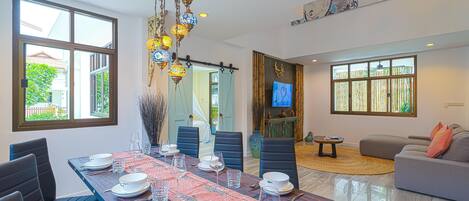 Comedor con una larga mesa dispuesta para seis personas, rodeada de sillas, una lámpara colgante decorativa y un amplio ventanal con vistas a zonas verdes.