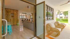 A modern interior with a glass door leading to a balcony, a dining area with a sofa, and wicker furniture. - Pool villa  4 BR walking to Beach HV (Hua Hin)