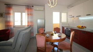 Une cuisine moderne avec des meubles blancs, une table à manger avec des chaises et un panier de fruits posé sur le comptoir.