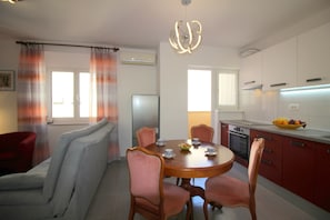 A modern kitchen with white cabinets, a dining table with chairs, and a fruit bowl on the counter. - Apartment Agata with sea view and close to the beach (Porec)