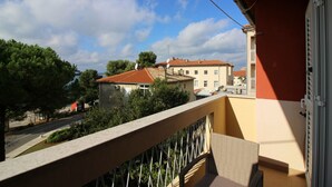 Un balcon donnant sur une rue, des immeubles et des arbres.