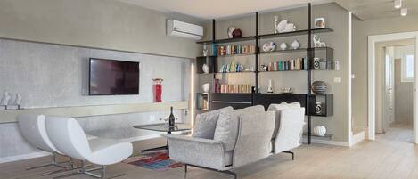 A modern living room with a flat-screen TV, a sofa, a coffee table, and a bookshelf.