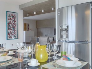 Uma cozinha moderna com geladeira de aço inoxidável, uma mesa de jantar posta com pratos, copos e um jarro amarelo.