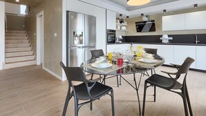 A modern kitchen with stainless steel appliances, a dining area with a glass table and black chairs, and a staircase leading to another level. - Villa Laura (Stanišovi)
