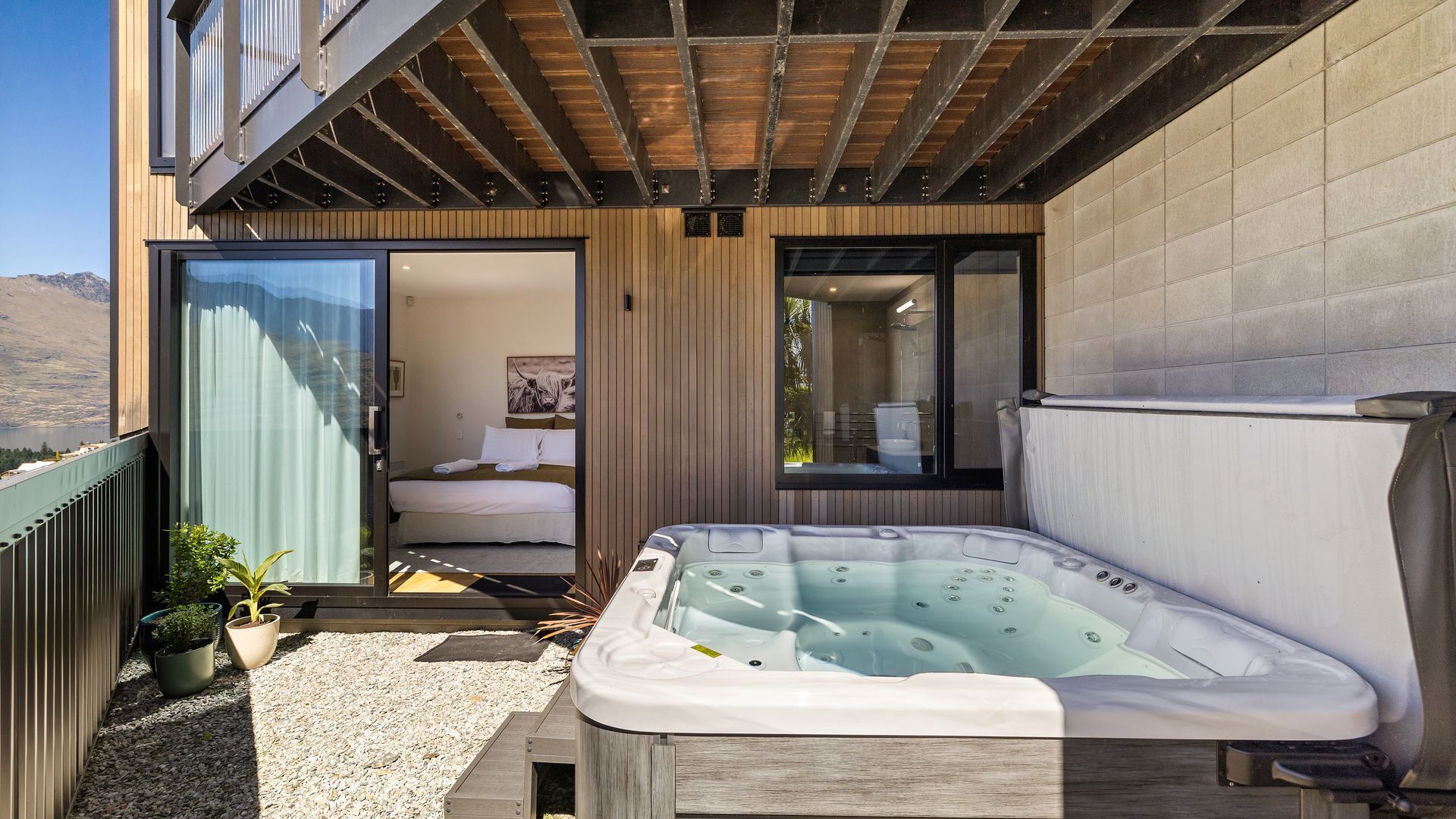 Un baño moderno al aire libre con un jacuzzi, una ducha y un dormitorio con un gran ventanal.