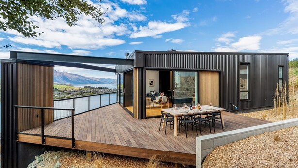A modern house with a deck, a dining area, and a view of mountains.