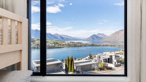 A bedroom with a large window offering a view of a lake, mountains, and a town.