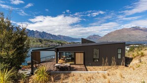 A modern house with a deck overlooking a lake and mountains.