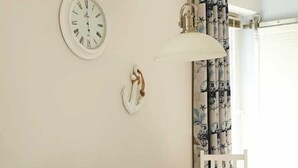 Un comedor con una mesa de madera, sillas blancas, un reloj de pared y una lámpara colgante.
