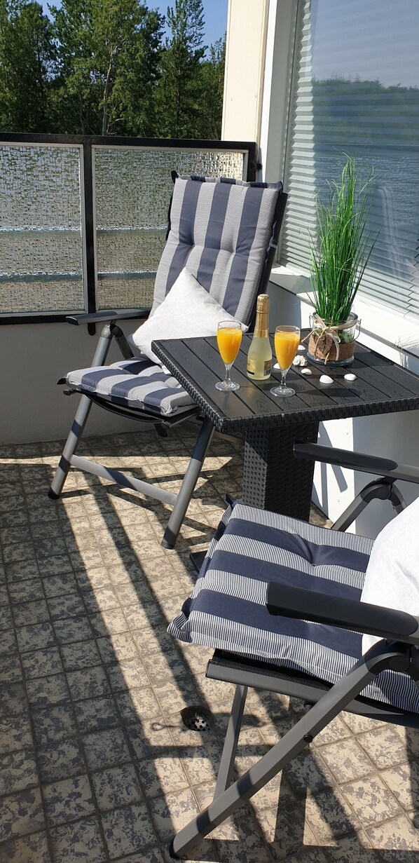 A balcony with two striped lounge chairs, a small table with drinks, and a potted plant.