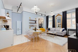 Un salon moderne avec un canapé, une table basse et des chaises transparentes. Il y a également un coin cuisine avec un réfrigérateur et une table à manger.