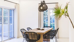 En matplats med ett träbord och svarta stolar, en hängande lampa och ett stort fönster med gardiner.