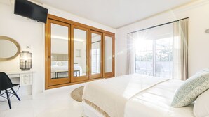 Ett sovrum med en stor säng, ett skrivbord, en stol, en garderob och en tv.