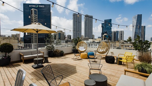 A rooftop terrace with outdoor furniture, potted plants, and a city skyline in the background. - Domus Metro Hotel (Tel Aviv)