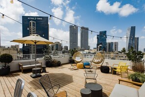 Une terrasse sur le toit, aménagée avec du mobilier d’extérieur, des plantes en pot, et offrant une vue sur le panorama urbain.