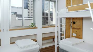 Quarto de hotel moderno com beliche, janela com vista para edifícios da cidade e estantes embutidas.