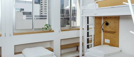 A modern hotel room with a bunk bed, a window with a view of city buildings, and built-in shelves.
