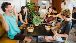 A group of people seated around a table with bowls of food, a potted plant, and a casual dining atmosphere. - Domus Metro Hotel (Tel Aviv)