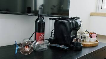 Un téléviseur à écran plat, une bouteille de vin, un verre à vin, une machine à café et une télécommande, le tout posé sur une table en bois.